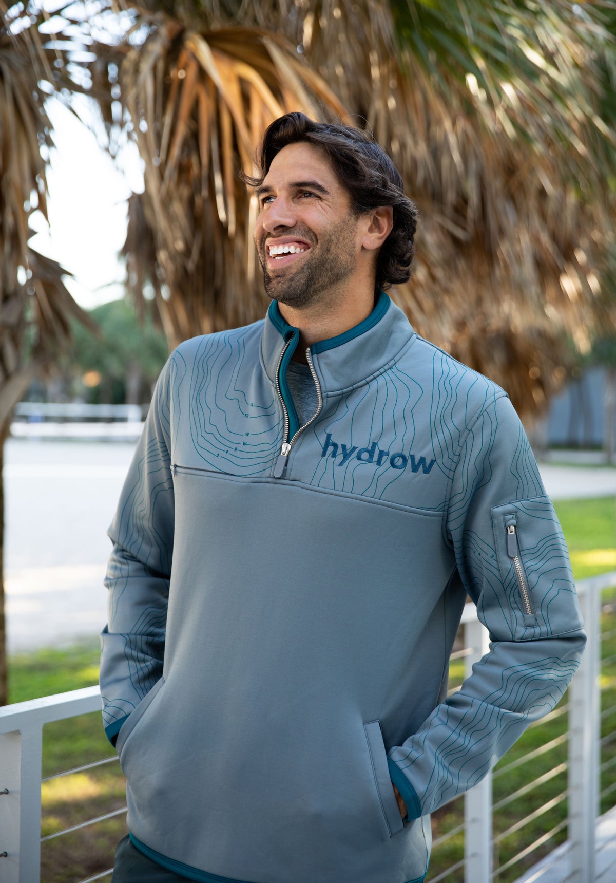 Man in grey 1/4 zip pullover with dark blue &quot;hydrow&quot; logo on left chest