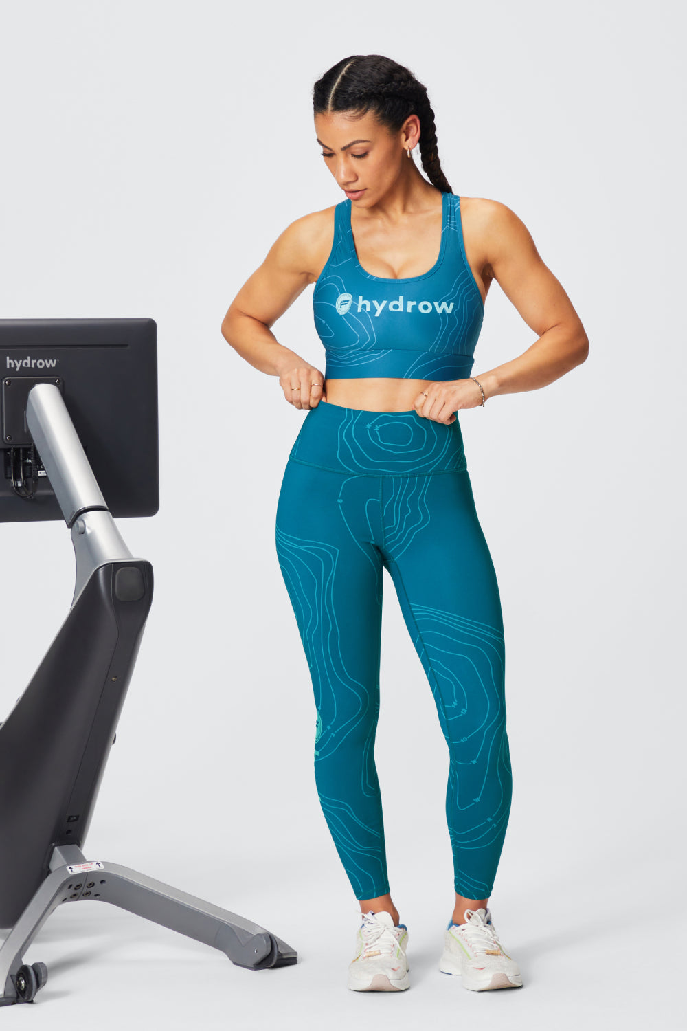 woman standing next to hydrow rower in the define powerhold high-waisted 7/8 leggings and the on-the-go medium impact sports bra